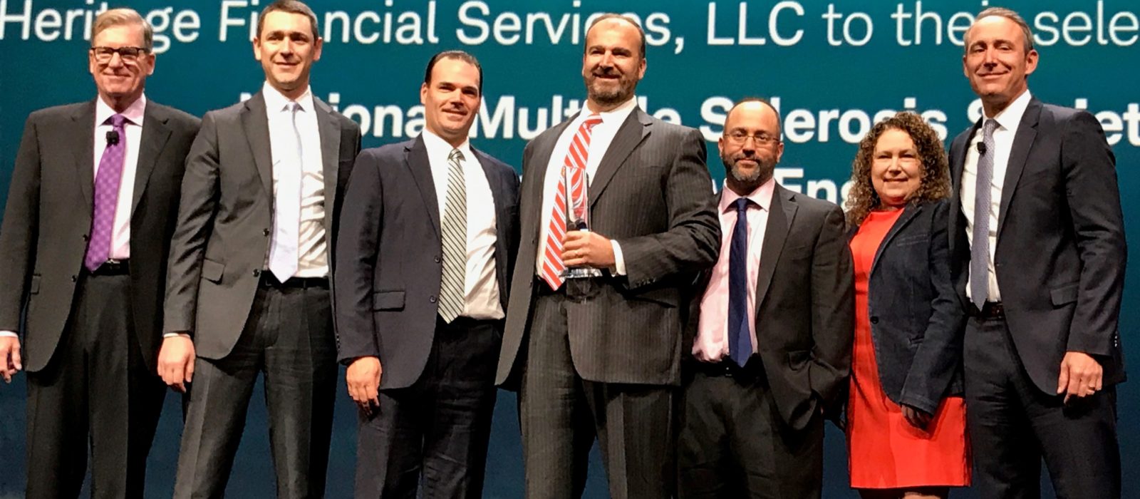 Heritage Financial Services Leadership a group of five individuals is standing on stage wearing business attire receiving the Schwab Impact Award, 2017